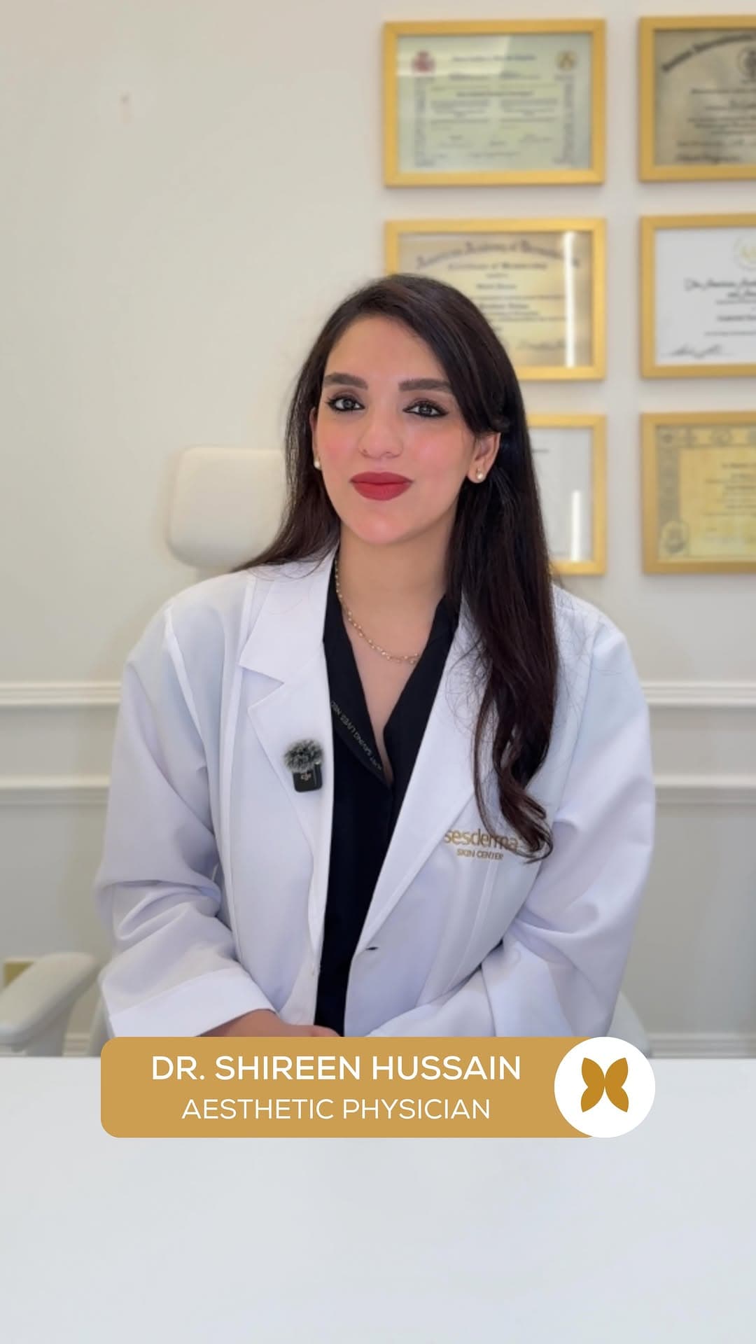 Dr. Shireen Hussain in a white coat in front of her framed medical certificates